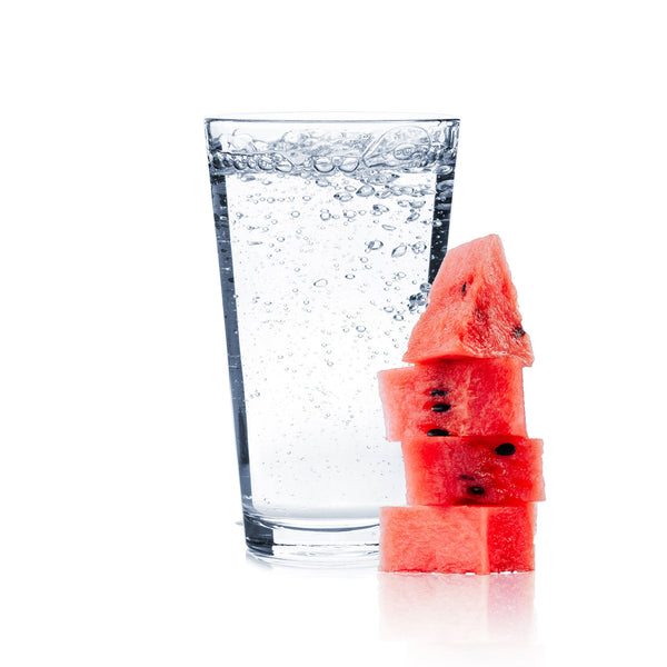 A glass of Watermelon Hard Seltzer with juicy watermelon slices next to it.