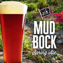 Glass of Amber Ale with 'Mud Bock Spring Ale' text in a garden with a stream