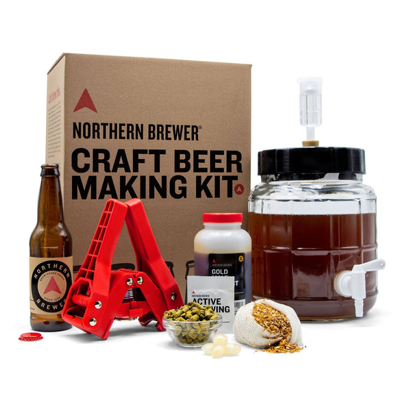 Fermentor with airlock, bottle capper, bottle, extract in a container, a bowl with hops, and a mesh bag with specialty grains